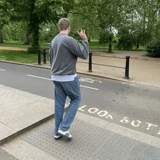 Liam crossing a road into a London park, throwing up a hand sign